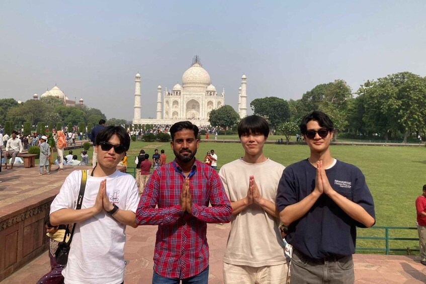 Four people standing in front of the Taj Mahal with their hands in a prayer position. 3