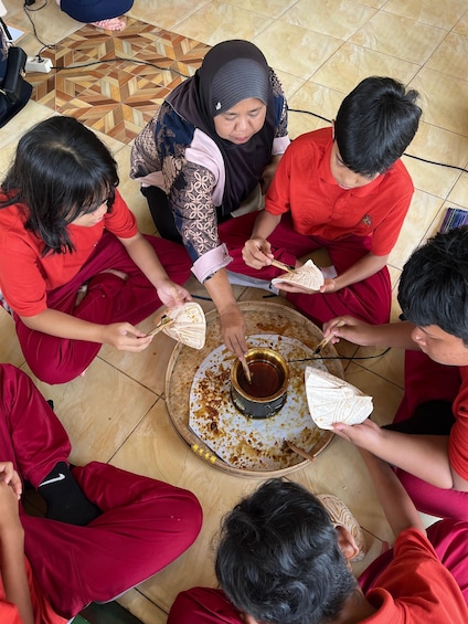 A group of people sitting in a circle on the floor, engaged in a communal activity involving a bowl of food. 4