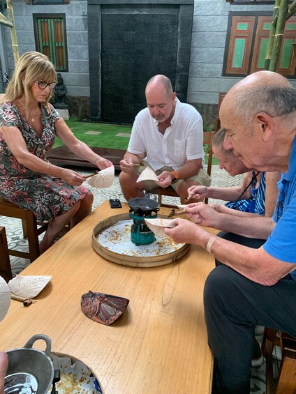 A group of people sitting around a table with a portable stove, engaged in a cooking activity. 5