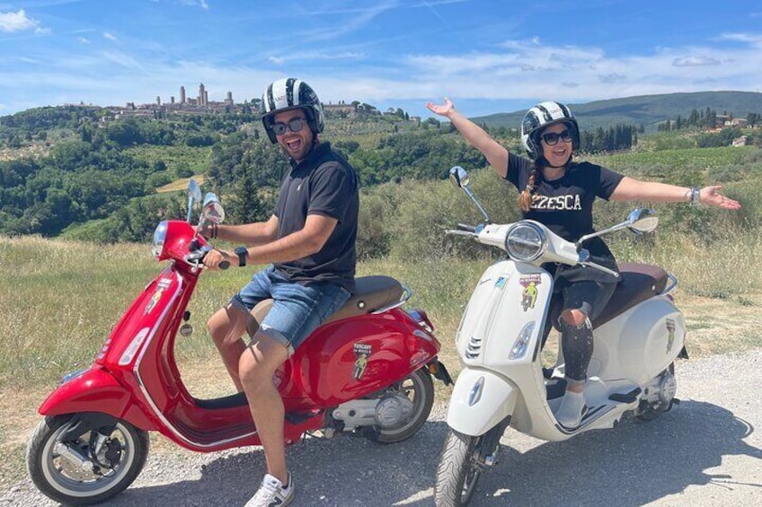 Dos personas en patinetas, una roja y otra blanca, en un área con césped y un castillo al fondo. 2