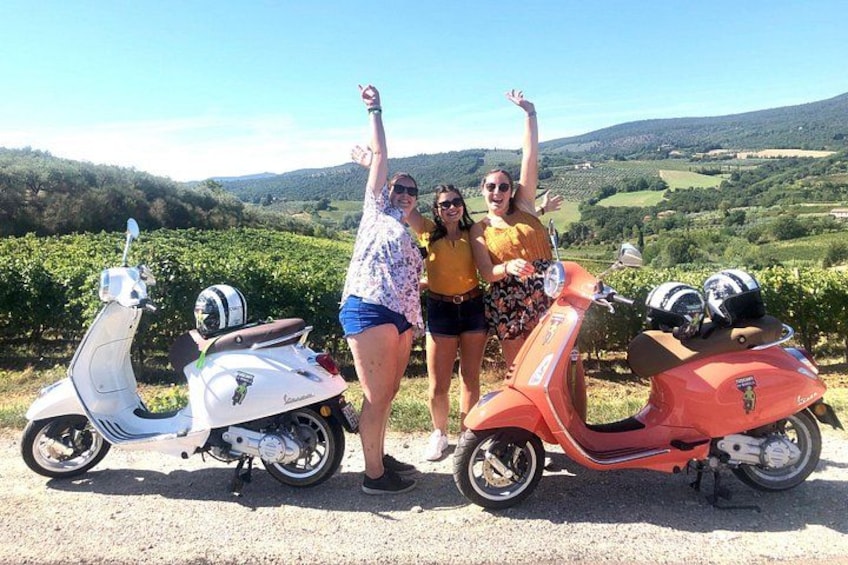 Two scooters, a white one and a red one, parked on a gravel path with a vineyard and hills in the background. 4