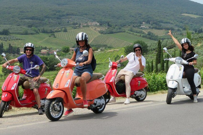 Three people on scooters on a road with a hilly landscape in the background. 3