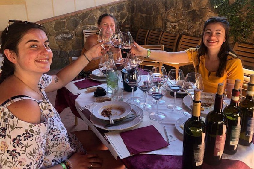 A group of people toasting with wine glasses at a table with bottles and plates. 5
