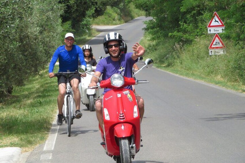 Three people riding bicycles and a red scooter on a road with road signs. 4