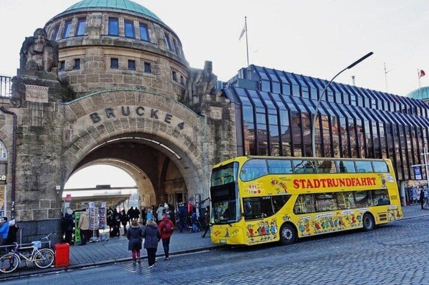 A double-decker bus labeled 'Stadtverkehr' at a historic archway with 'Brucke' inscribed on it. 4