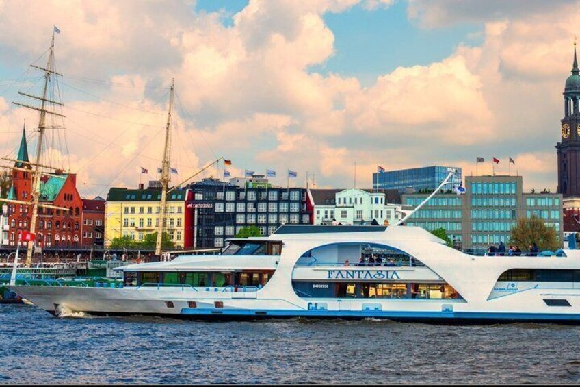 A modern yacht with 'FANTASIA' written on its side, docked near a historic cityscape with colorful buildings and a clock tower. 3