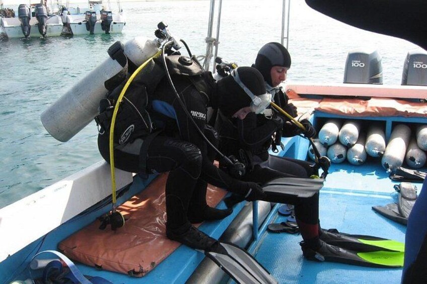 Un buzo con equipo de escafandra autónoma en un bote, rodeado de tanques y equipos de buceo. 3