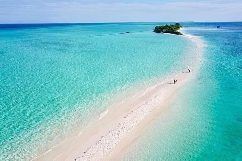 Een strand met helder turquoise water, een zandstrand en een klein eiland in de verte. 1