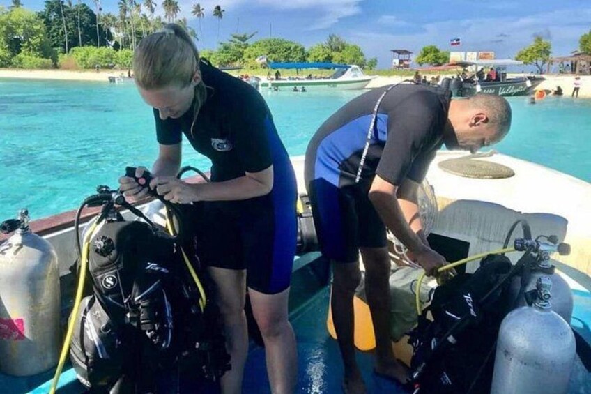 Dos personas preparando equipo de buceo en un bote cerca de una playa. 5