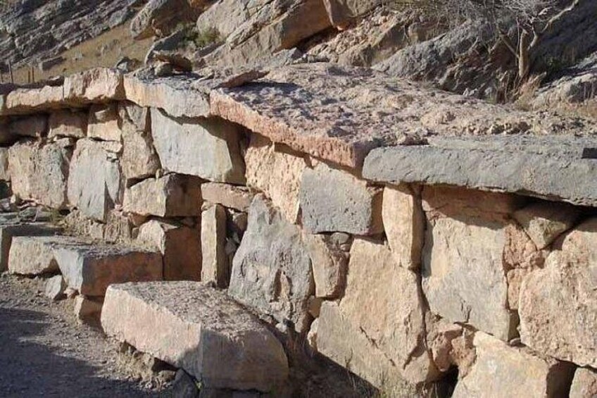 A stone wall with unevenly cut stones and a rugged hillside in the background. 3