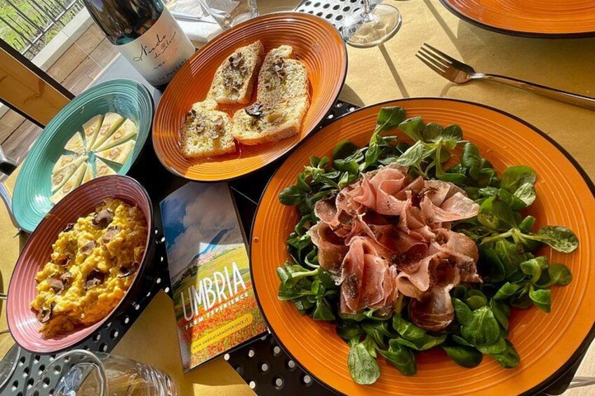 Une table avec des assiettes de nourriture, notamment une salade au jambon de Parme, un plat de pâtes et une assiette de pain. 2