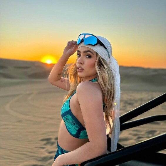 A person in a bikini on a beach with sand dunes and a sunset in the background. 1