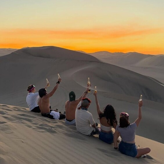 A group of people sitting on sand dunes at sunset. 4