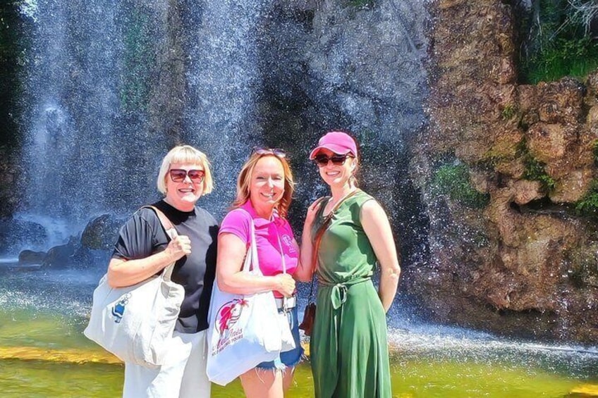 Tre persone in piedi di fronte a una cascata, con acqua che scorre su rocce. 4