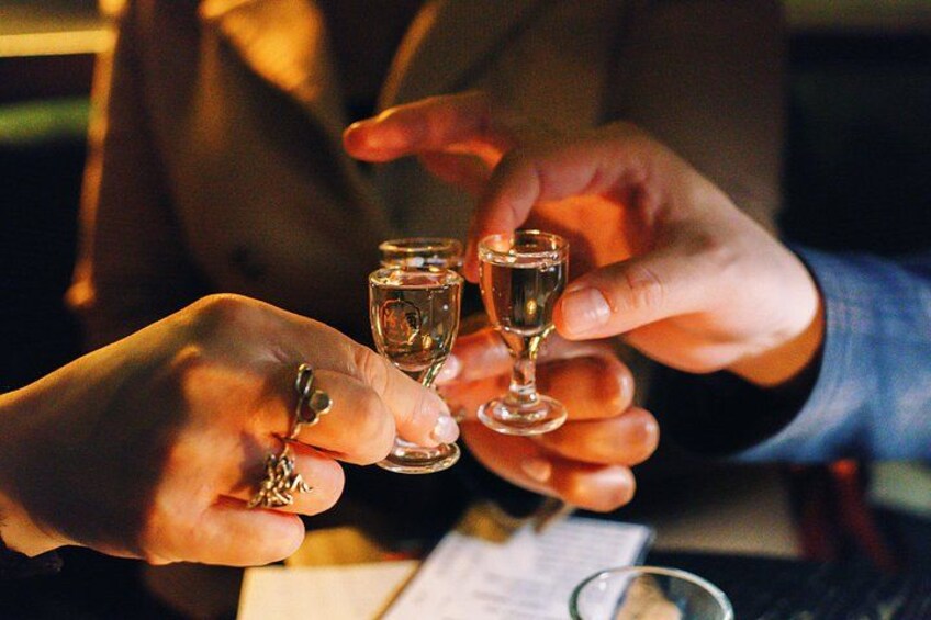 Hands holding a small glass and a larger glass, possibly in a social setting. 3
