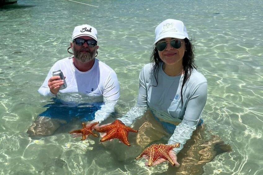 Two people holding starfish in clear shallow water. 4