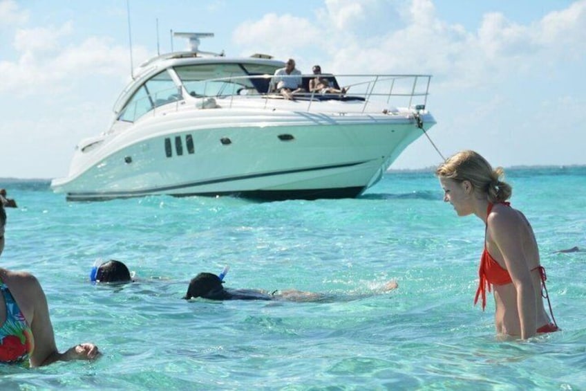A yacht with people on board, a person swimming, and another person standing in the water. 1