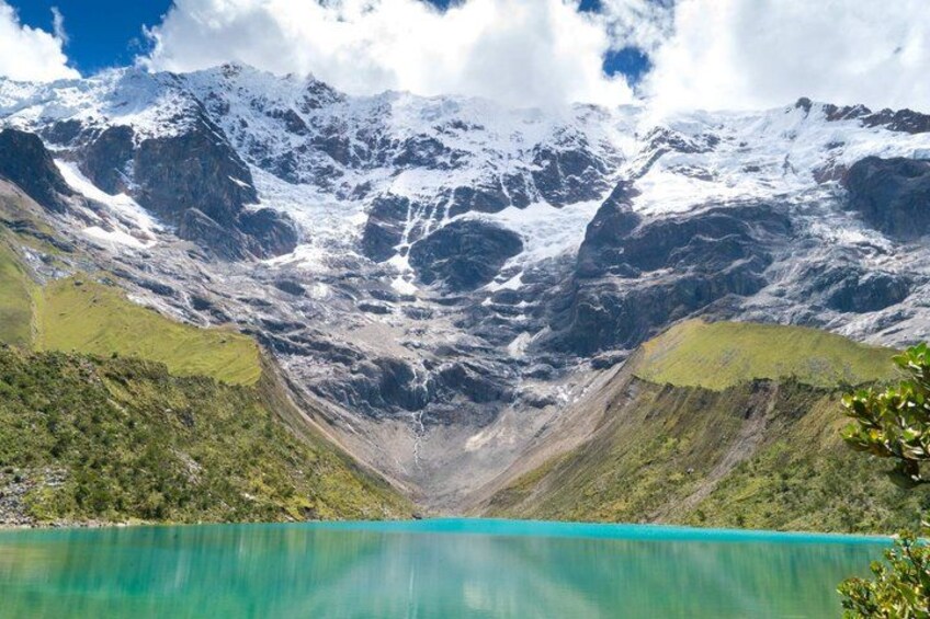A mountain range with snow-capped peaks, a turquoise lake, and green vegetation. 1