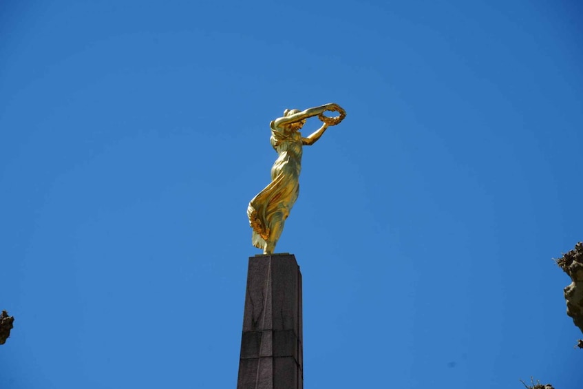 A golden statue of a woman on a pedestal against a clear blue sky. 1