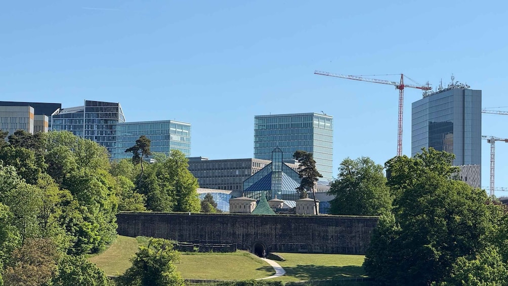A cityscape with modern buildings, a construction crane, and a historic stone wall. 2