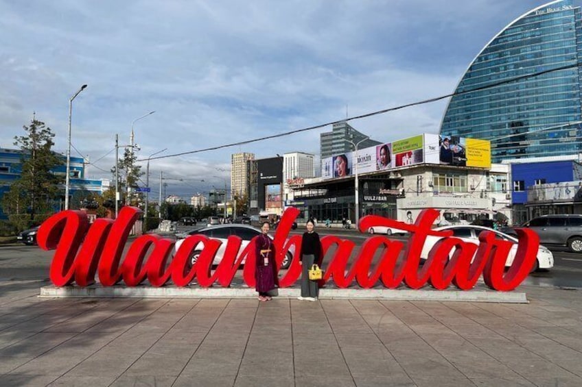 Un grand panneau rouge avec le mot « Wagonerator » bien visible au premier plan, un bâtiment moderne à la façade en verre incurvée en arrière-plan, et une rue avec des voitures et des piétons. 1