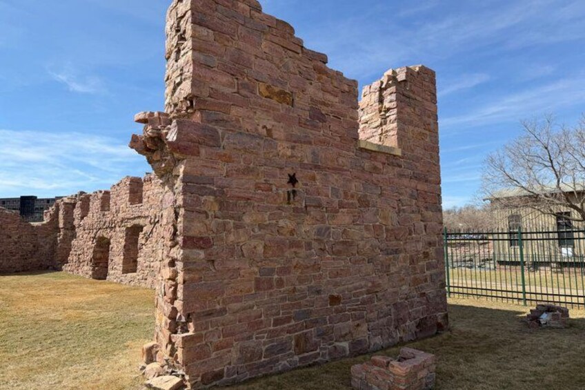 A historical brick structure with partial walls and a fenced area. 1