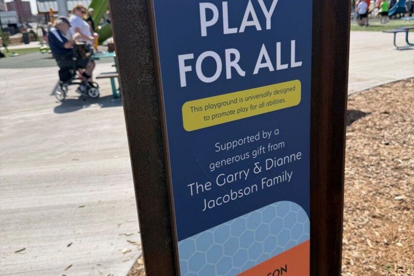 A playground sign with the text 'PLAY FOR ALL' and mentions support from The Garry & Dianne Jacobson Family. 2