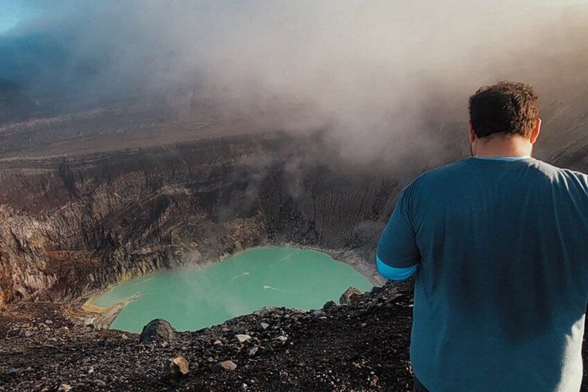 A person overlooking a large crater with a turquoise lake surrounded by volcanic terrain. 5