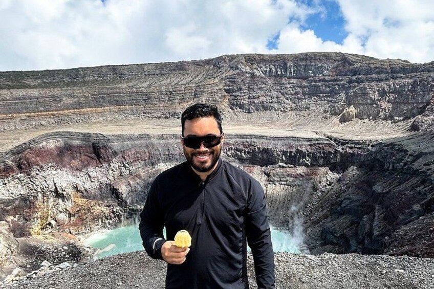 A person holding an ice cream cone in front of a large, rugged landscape with layered rock formations and a small body of water. 2
