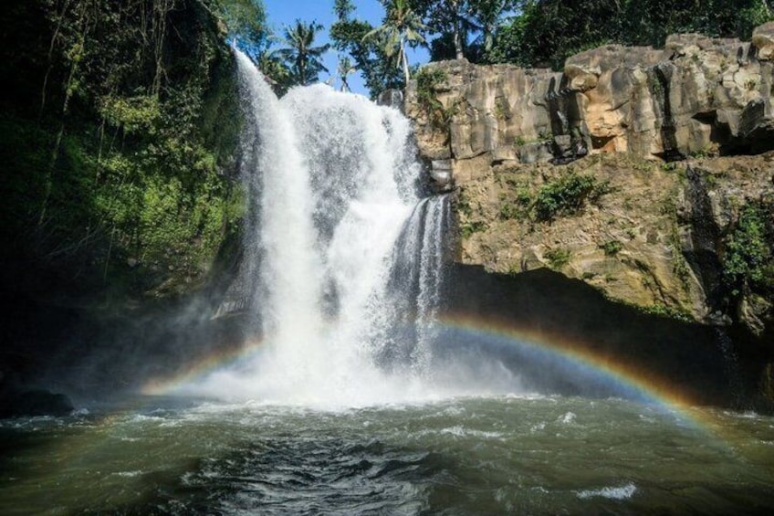 Une cascade surmontée d’un arc-en-ciel, entourée de verdure et de falaises rocheuses. 3