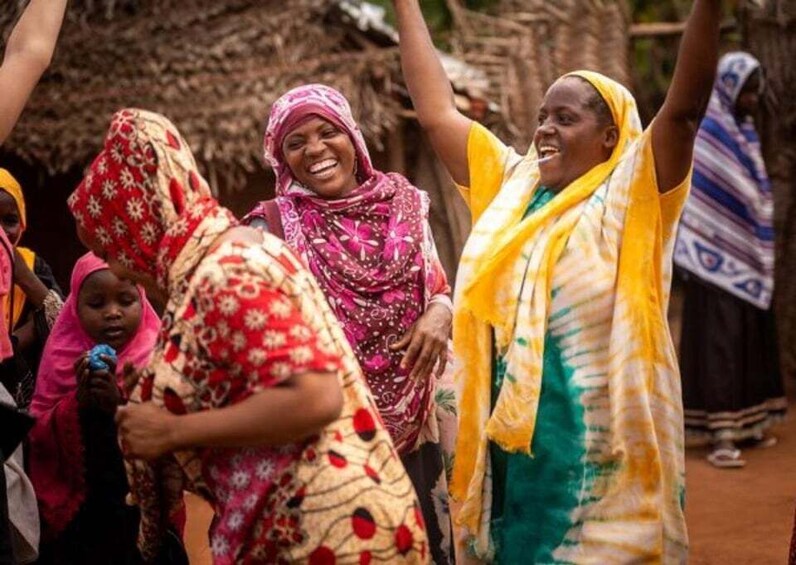 A group of people in traditional attire, gathered in an outdoor setting with thatched structures in the background. 4