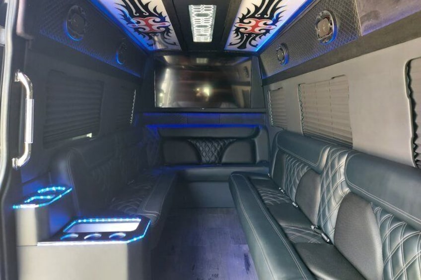 A van interior with leather seating, blue ambient lighting, and decorative wall panels. 3