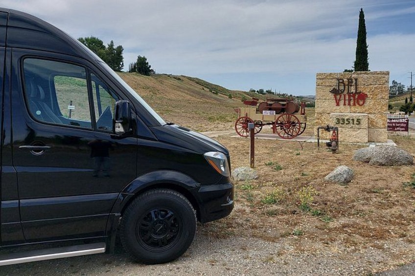 A black van parked on a gravel road with a historical carriage and a stone sign in the background. 2