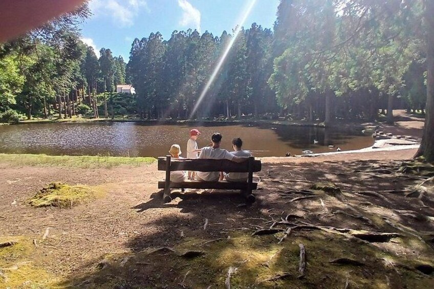 Un groupe de personnes est assis sur un banc, près d’un lac bordé d’arbres. 1
