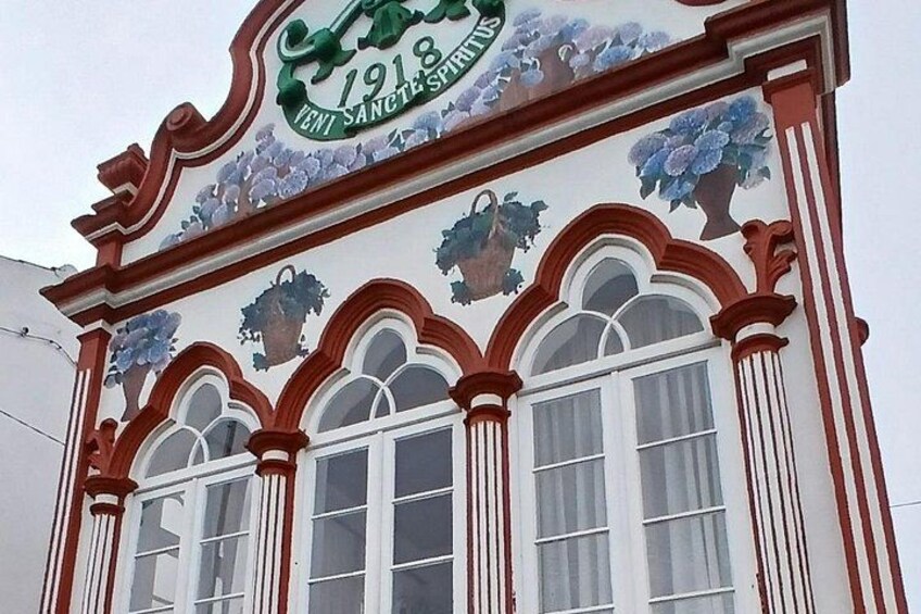 Un bâtiment orné de motifs rouges et blancs, avec une enseigne verte portant l’année 1918 et des motifs floraux décoratifs. 4