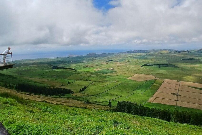 Un paysage vallonné, avec des collines, des champs, et une personne debout sur une plateforme. 5