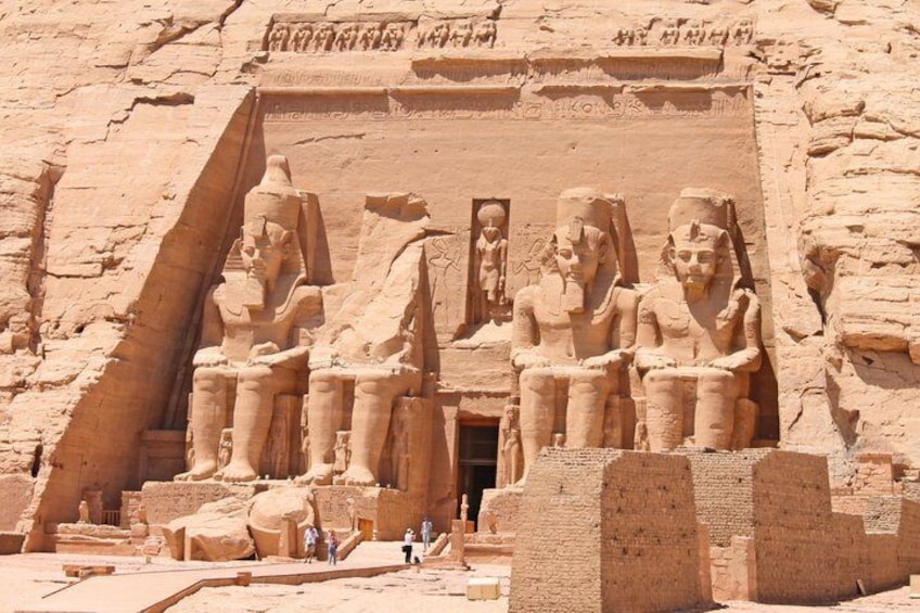 A large sandstone temple with colossal statues of seated figures, a large doorway, and hieroglyphic inscriptions. 1