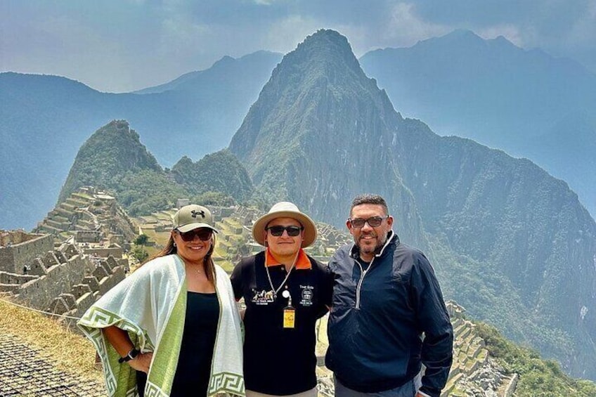 Tres personas frente a Machu Picchu, con las ruinas de la montaña al fondo. 1