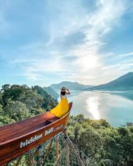 A wooden boat with a person in a yellow outfit on a calm lake surrounded by lush greenery and mountains. 2