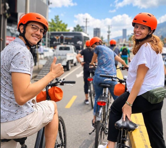 People on bicycles with orange helmets on a city street. 4