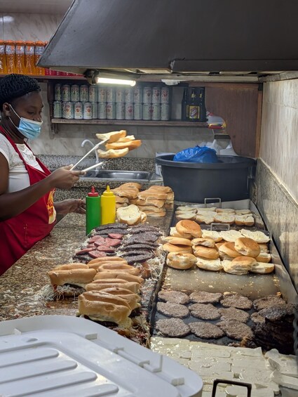 A street food vendor grilling various foods, including sausages and bread, with condiments and cooking utensils visible. 4