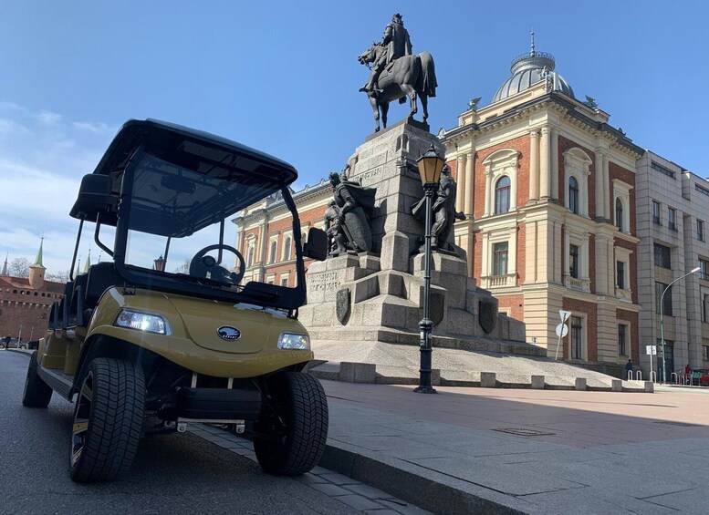 Keltainen golfauto on pysäköitynä patsaan ja rakennuksen eteen. 1