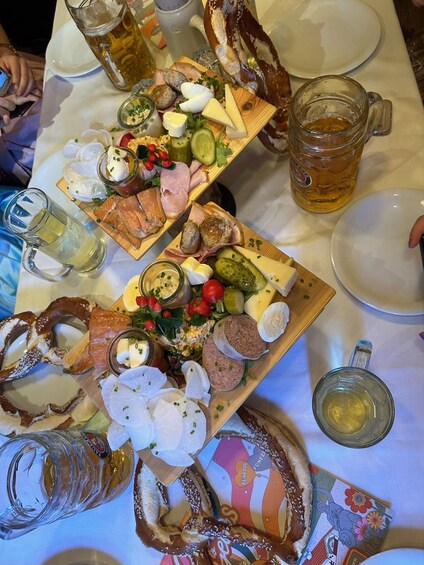 A table with various food items, including meats, cheeses, and pickles, along with several beer mugs. 4