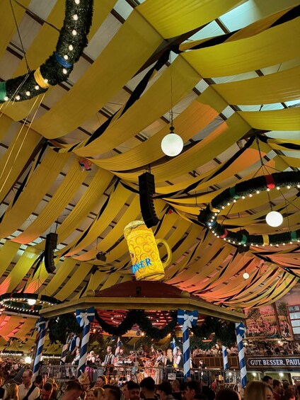 A festive market with yellow drapes, a beer mug decoration, and a crowd. 1