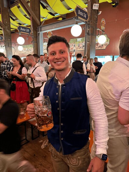 A person holding a beer mug in a crowded indoor setting with visible signs indicating 'Boxe 14' and 'Boxe 20'. 3