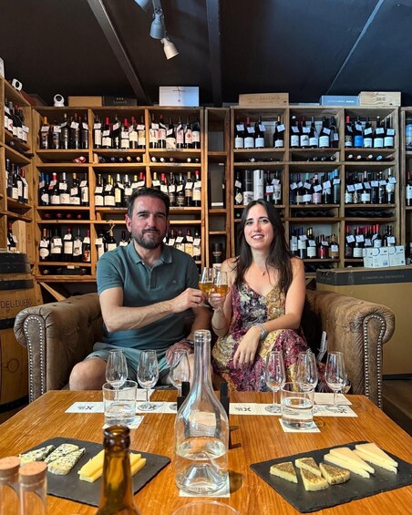 Two people seated at a table with wine glasses and bottles in a wine cellar. 3