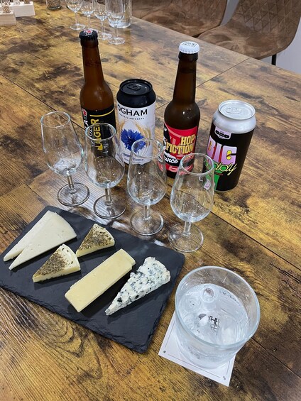 A wooden table with various food items, including cheese, beer bottles, and a can of soda. 5