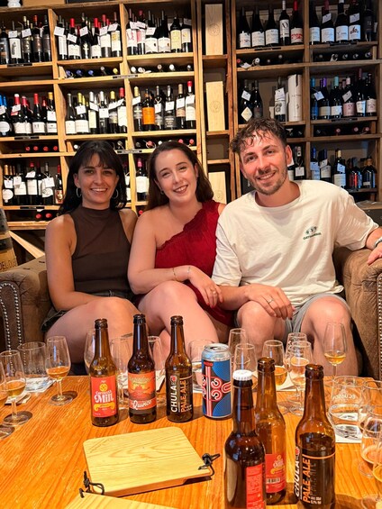 Three people seated on a couch in a room with a wine rack in the background. 2