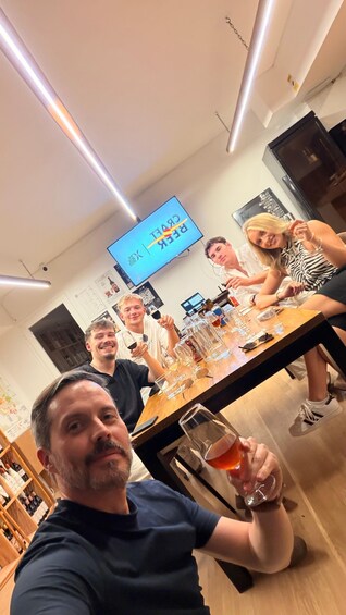 A group of people sitting at a table with glasses and bottles, in a room with a TV displaying 'BILLBOARD' and 'GREAT'. 4