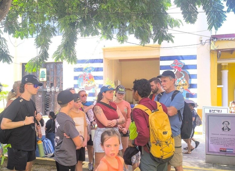 A group of people standing outdoors, some with backpacks, in front of a building with a signboard. 4